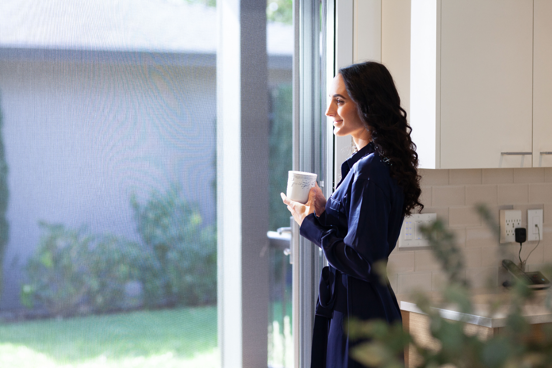 Woman enjoying morning coffee by Mirage 3500 retractable screen in modern kitchen